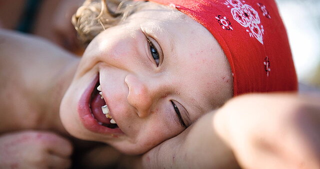 Ein Mädchen mit Zahnlücke und rotem Kopftuch lächelt in die Kamera